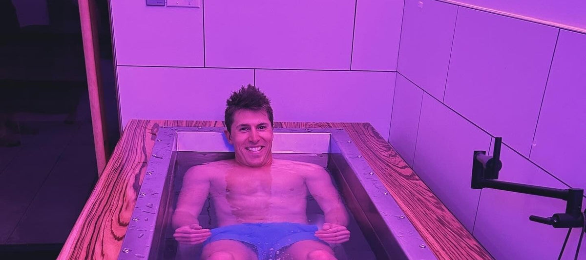 Smiling man immersed in a zebrawood-decked BlueCube C2 cold plunge at a gym