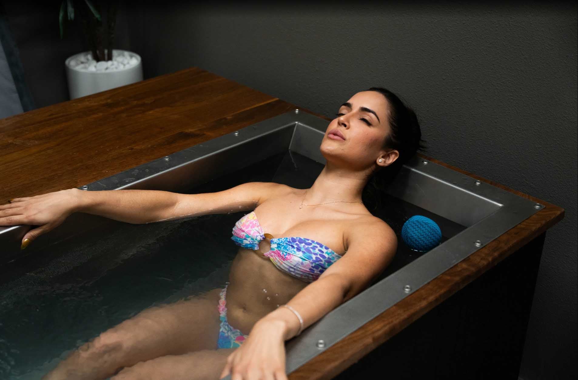 Woman fully immersed in a custom BlueCube C3 cold plunge with black walnut deck at Project Wellbeing in Las Vegas, NV