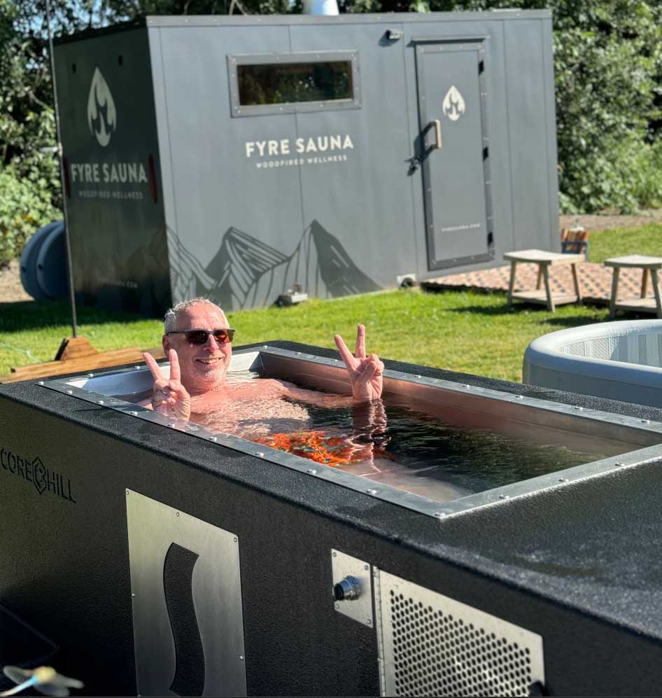 Man giving peace signs in a custom BlueCube C2 black cold plunge with stainless steel decal at Fyre Sauna in Redmond, WA