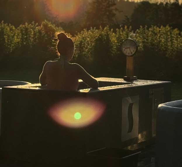 Woman silhouetted at sunset in a custom BlueCube C2 black cold plunge with stainless steel decal at Fyre Sauna in Redmond, WA